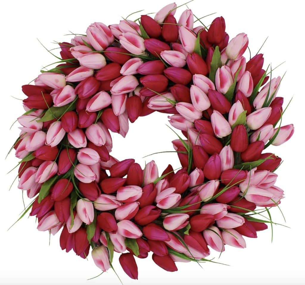 A circular wreath crafted with tightly packed pink and red tulips, accented by lush green leaves in an alternating pattern. The evenly distributed tulips create a vibrant and colorful floral display, showcasing the beauty of pink crafts against a pristine white background.